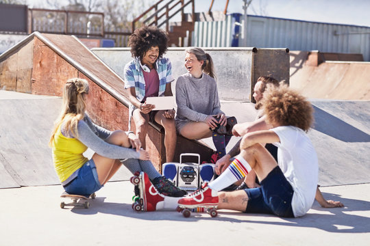 Friends in roller skates on skateboard using digital tablet at sunny skate park