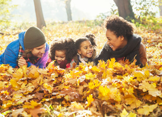 Playful young family laying in autumn leaves in sunny woods