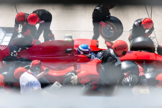 Manager stopwatch timing pit crew replacing tires on formula one race car in pit lane