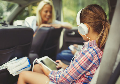 Girl headphones using digital tablet watching video in back seat of car