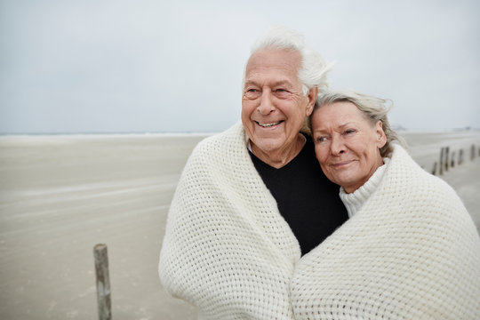 Smiling affectionate senior couple wrapped in a blanket on beach