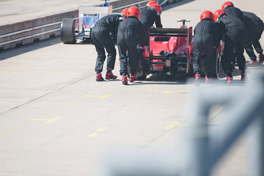 Pit crew pushing formula one race car out of pit lane