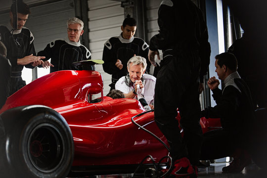 Manager pit crew working on formula one race car in dark repair garage