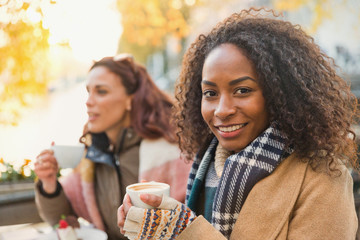 Portrait smiling young woman in warm clothing drinking espresso at sidewalk cafe
