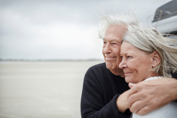 Affectionate senior couple hugging and looking away on beach