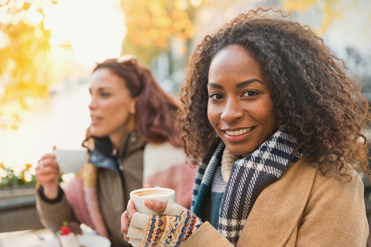 Portrait smiling young woman in warm clothing drinking espresso at sidewalk cafe