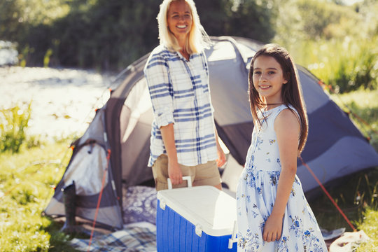 Portrait smiling mother daughter carrying cooler outside sunny campsite tent