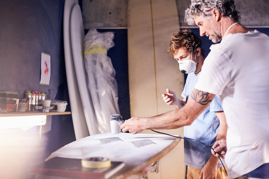 Male surfboard designers wearing protective masks sanding surfboard in workshop