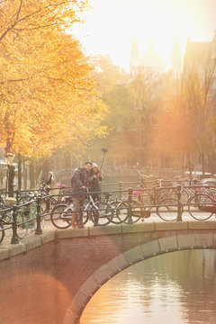 Young couple bicycles taking selfie selfie stick on bridge over canal in Amsterdam