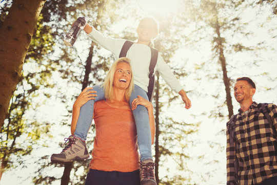 Mother carrying daughter on shoulders hiking in sunny woods