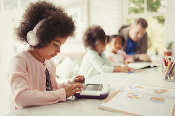 Girl with headphones using digital tablet doing homework at table