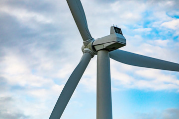 A low angle and close up shot on the nacelle, cover housing of generating components, of a wind turbine with three blades against a broken cloud sky - obrazy, fototapety, plakaty
