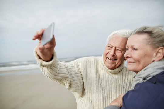 Senior couple taking selfie with cell phone on windy winter beach