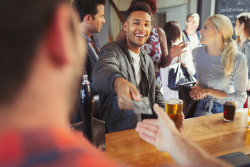 Smiling man paying bartender with credit card at bar