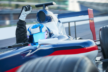 Portrait formula one race car driver wearing helmet cheering fist on sports track