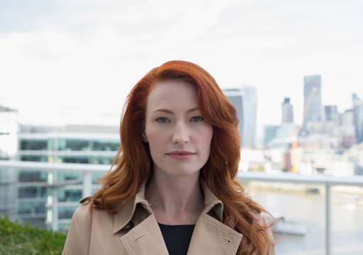 Portrait serious, confident businesswoman red hair on urban balcony city view