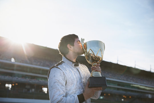 Male formula one driver kissing trophy, celebrating victory on sports track