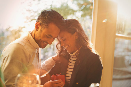 Affectionate, romantic boyfriend giving gift to girlfriend in sunny cafe - Powered by Adobe