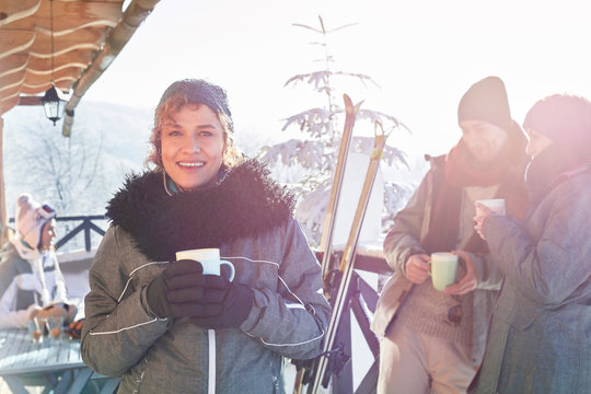 Portrait smiling female skier drinking coffee on cabin deck friends apres-ski