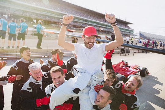 Formula one racing team carrying driver on shoulders, celebrating victory on sports track