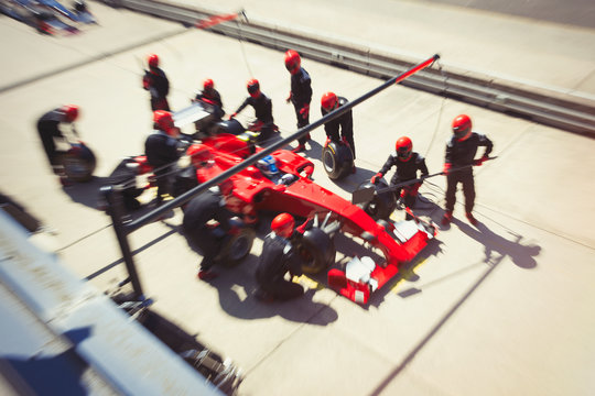 Pit crew replacing tires on formula one race car in pit lane