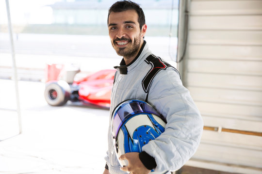 Portrait Confident Male Formula One Race Car Driver Holding Helmet In Repair Garage
