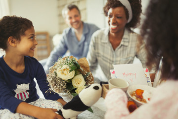 Daughters serving breakfast flowers to mother in bed on Mother’s Day
