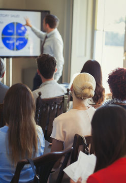 Business people in audience watching businessman leading conference presentation at television screen