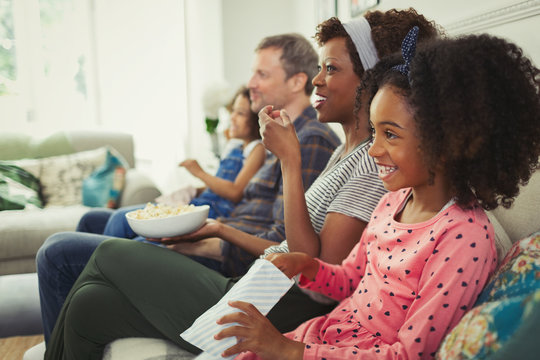 Young multi-ethnic family watching movie and eating popcorn on sofa