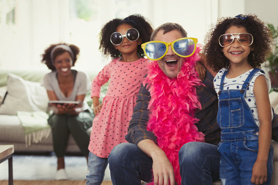 Portrait playful multi-ethnic father daughters playing dress up sunglasses feather boas