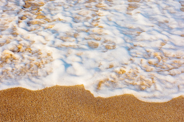 sea waves splash foam on the sunny beach.  mess of salt water and sand in evening light. dynamic nature texture