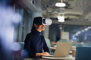 Businesswoman using virtual reality simulator at laptop in dark office