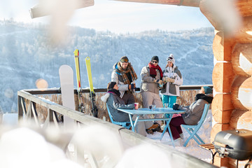 Skier snowboarder couples hanging out on sunny cabin balcony apres-ski