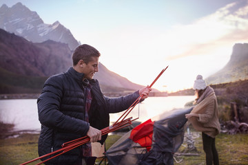 Young couple pitching tent at mountain lakeside campsite