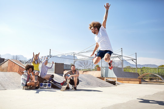 Friends watching cheering man jumping in roller skates at sunny skate park