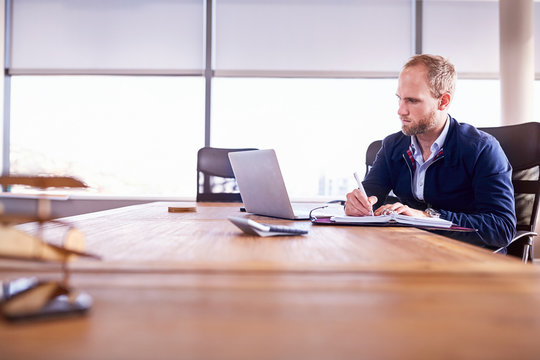 Focused businessman taking notes at laptop in conference room