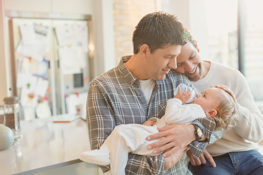 Affectionate male gay parents holding baby son with bottle