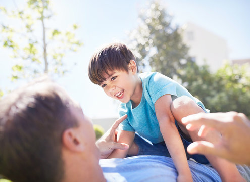 Laughing son laying on top of father on sunny patio
