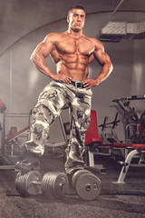 Fototapeta na wymiar Standing Strong. Bodybuilder Standing in front of Heavy Dumbbells at the Gym