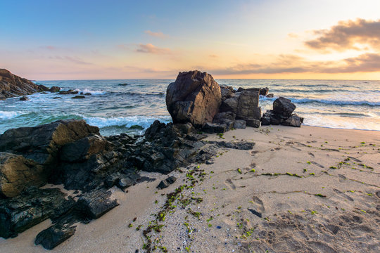 sea beach at sunrise. calm waves wash huge rocks. golden clouds on the sky. stunning marine scenery in morning light.