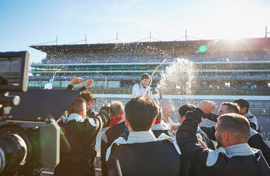 Formula one racing team spraying champagne on driver, celebrating victory on sports track
