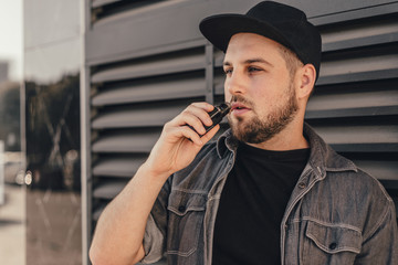 Young handsome man smoke with vape near black wall