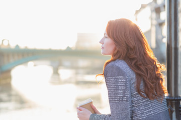 Serene businesswoman with red hair drinking coffee at urban waterfront