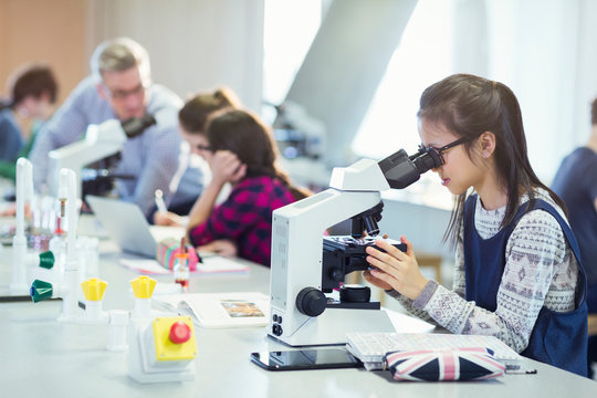 Girl student using microscope, conducting scientific experiment in laboratory classroom