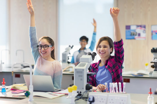 Eager, smiling students raising hands in science laboratory classroom
