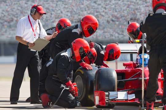 Manager stopwatch timing pit crew replacing formula one race car tire in pit lane