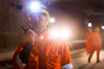 Male foreman headlamp using walkie-talkie at dark construction site