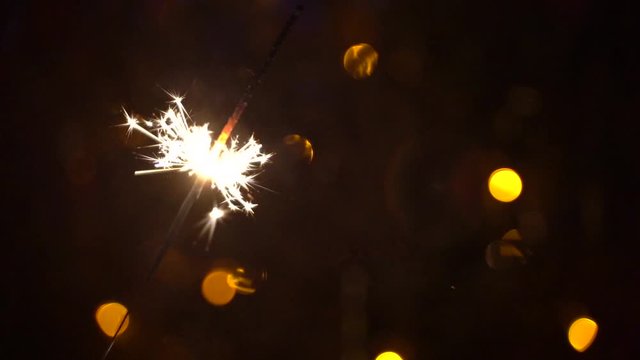 Bright gold sparks shoot form a sparkler on the background of multi-colored lights in slow motion. Celebrating the holiday, fun, joy, amazing atmosphere