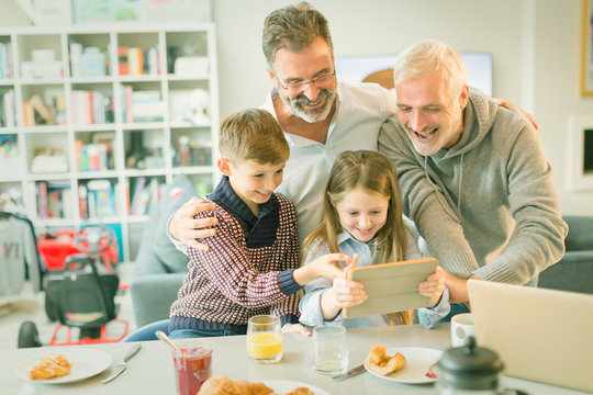 Male gay parents children video messaging digital tablet in morning kitchen