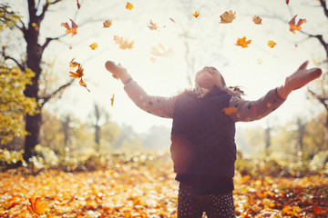 Playful girl throwing autumn leaves overhead in sunny park